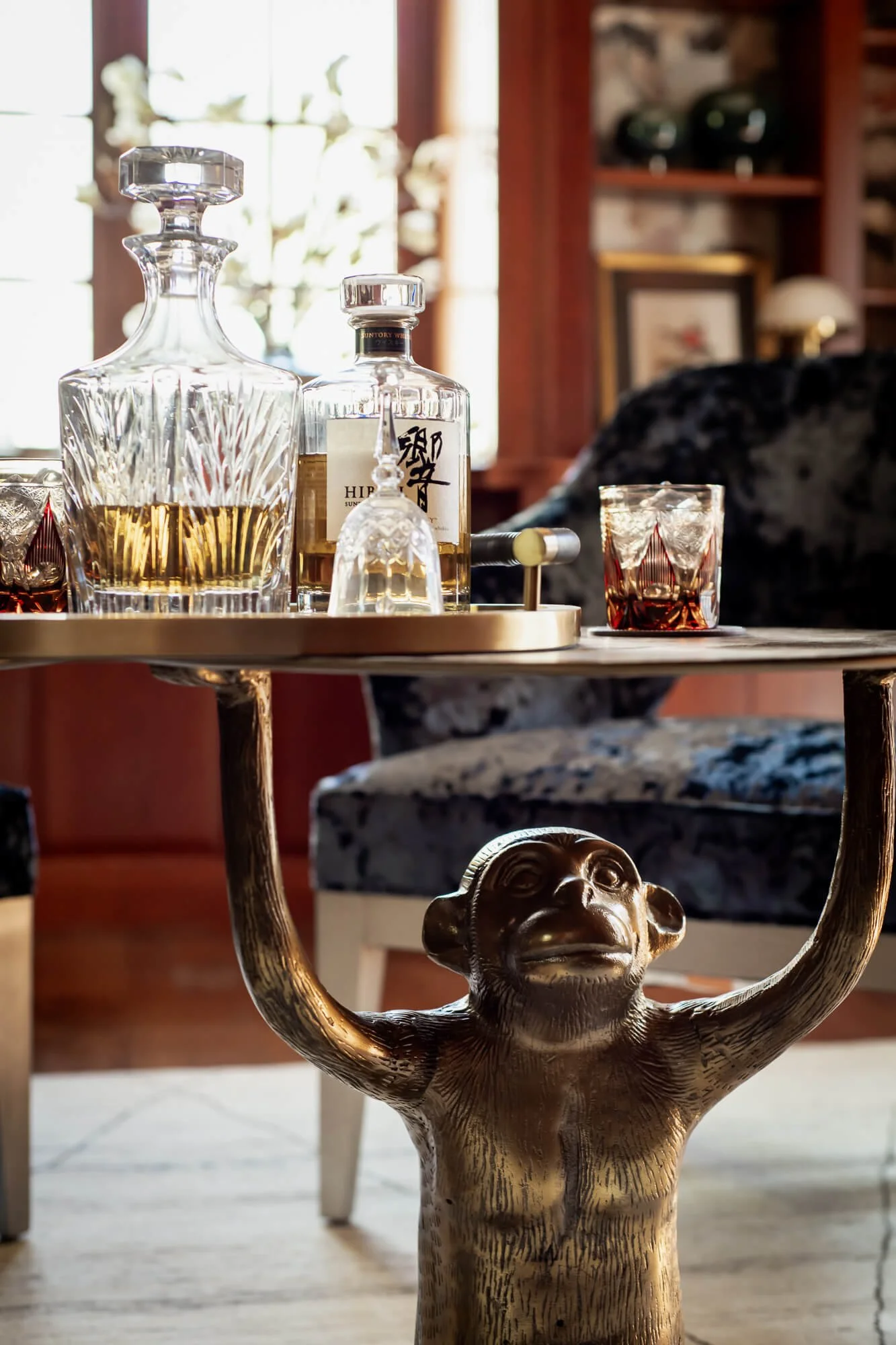 Close-up of a coffee table with a brass monkey base holding up the table. On top is glassware. 