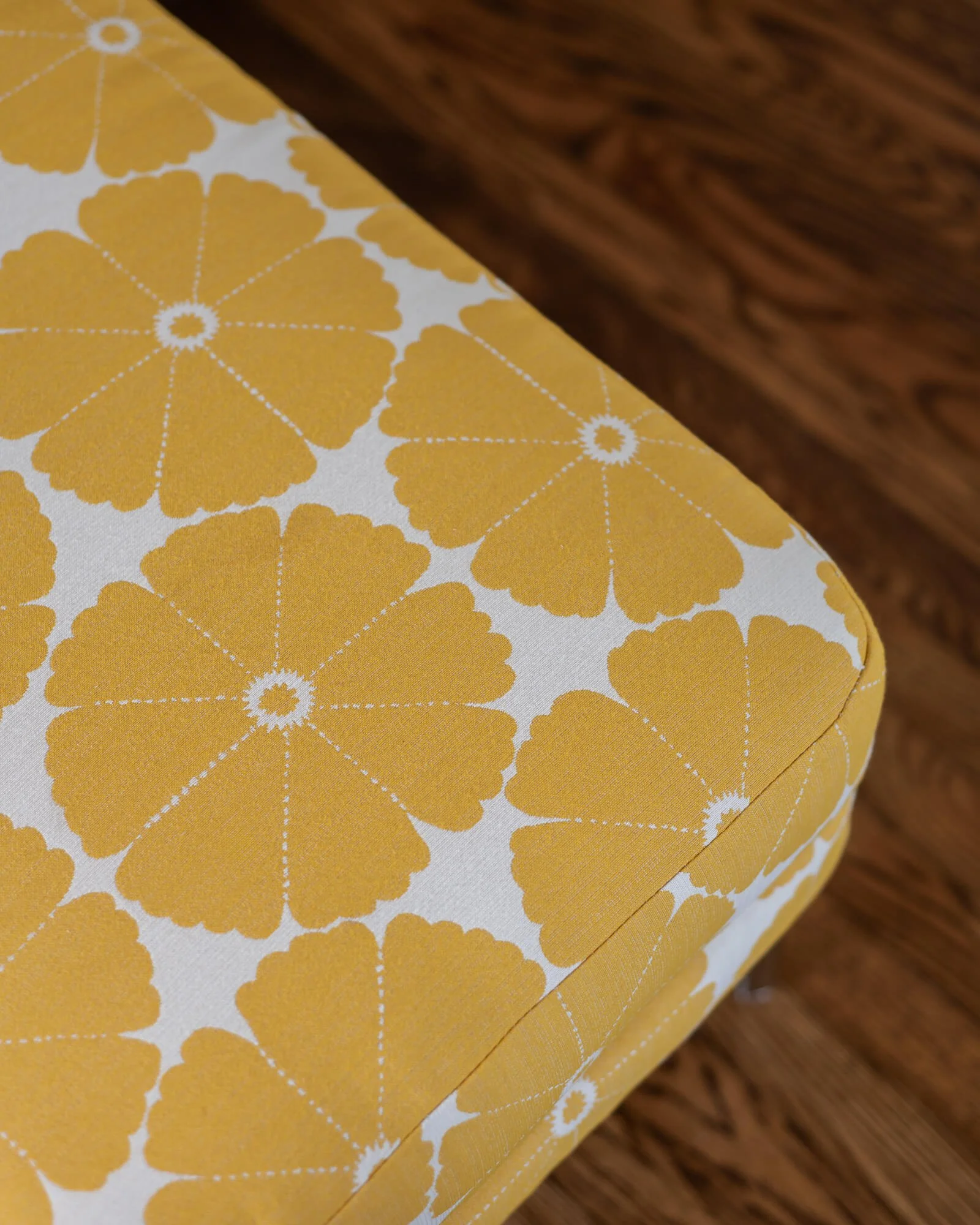 Close-up of a yellow and white patterned bench cushion fabric with floral designs on a wooden surface. 