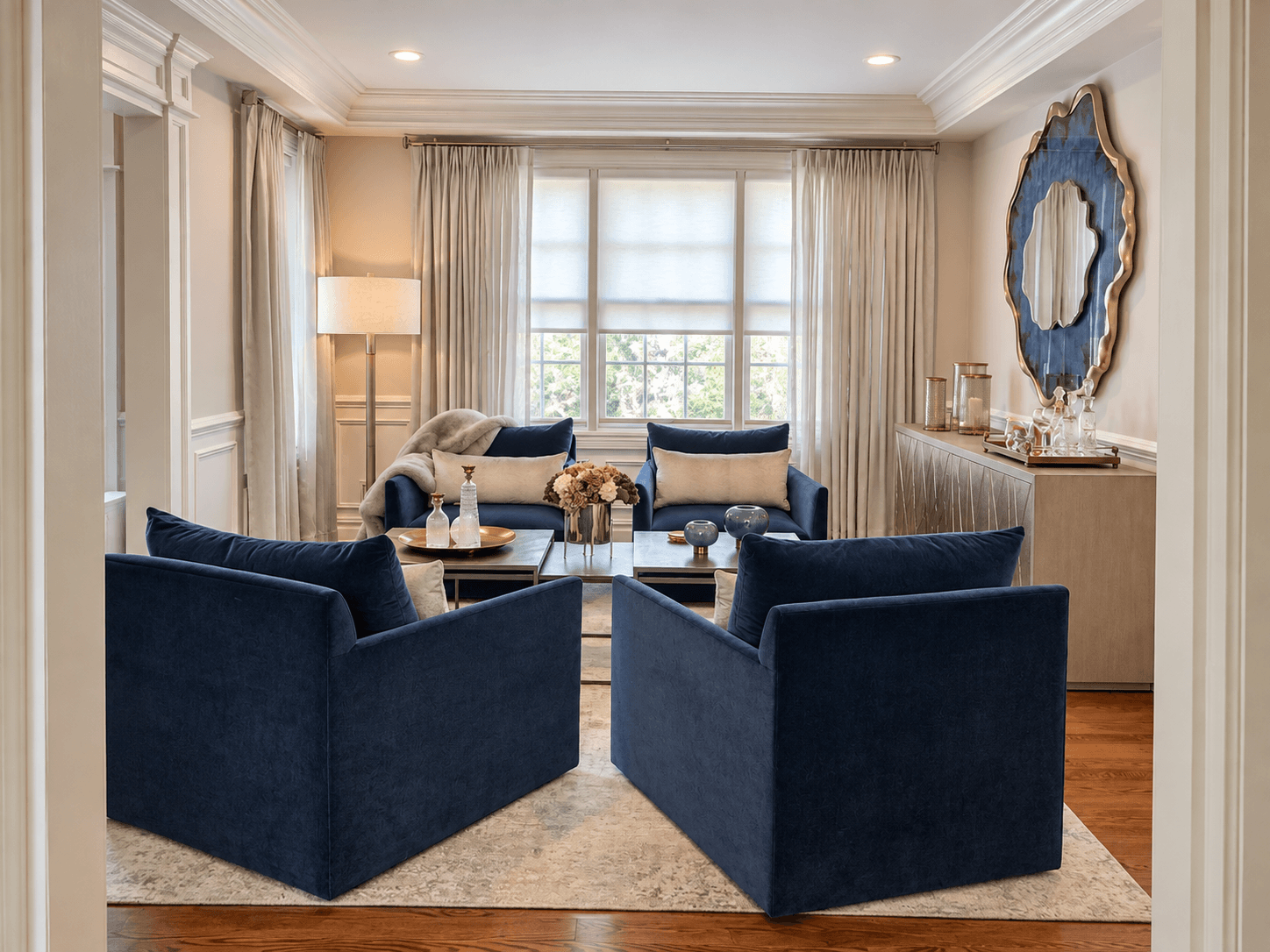 Living room design project in Scotch Plains, NJ by Elements Interior Design Studio featuring a modern statement blue and gold mirror on the wall above a metallic console table. The table has decor objects on top. There are 2 nesting brass coffee tabl