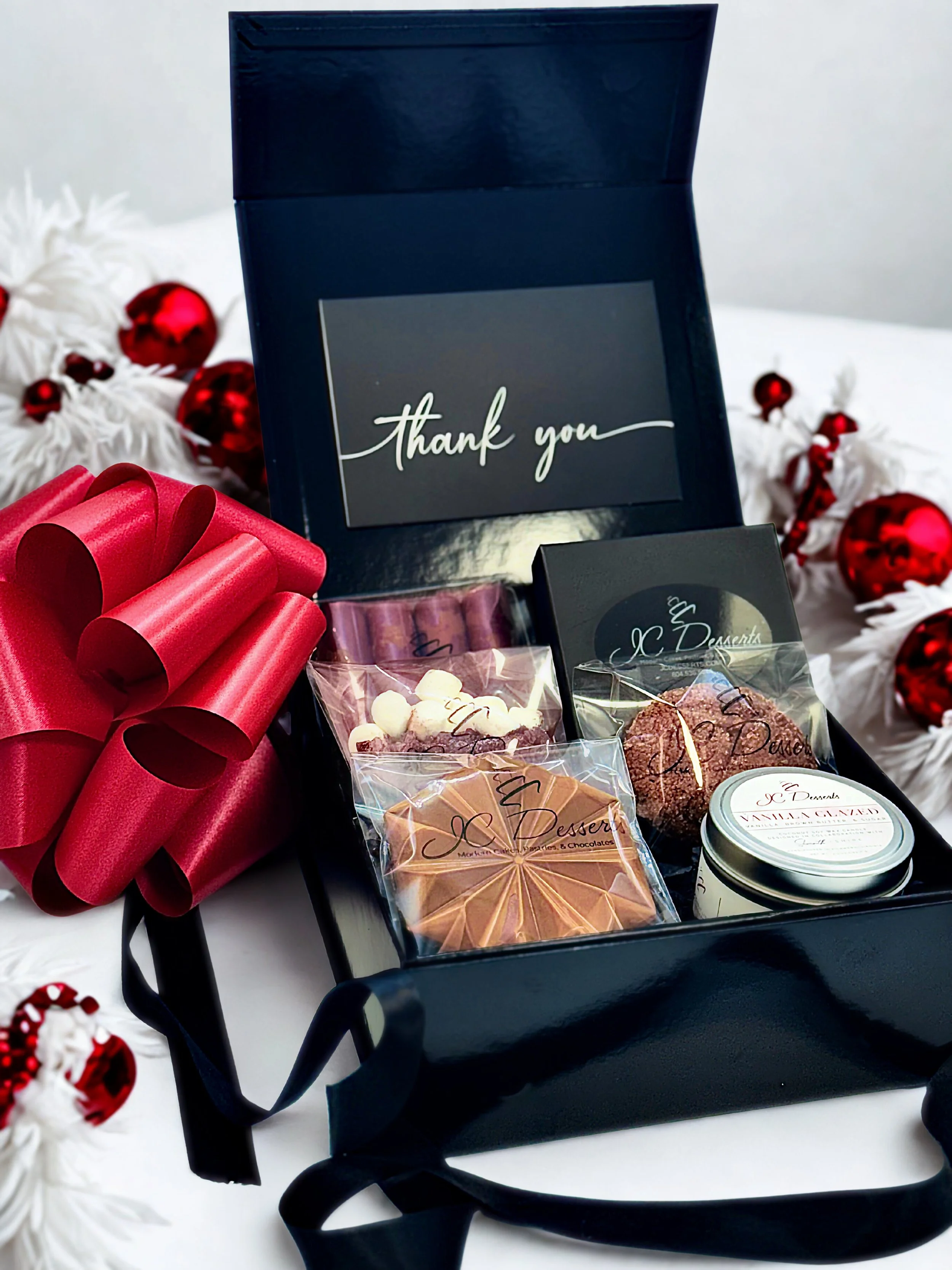 A premium black box gift set featuring assorted chocolate boxes, gourmet snacks, hot cocoa mix, a signature candle, and elegant keepsakes from JC Desserts in Richmond, VA.
