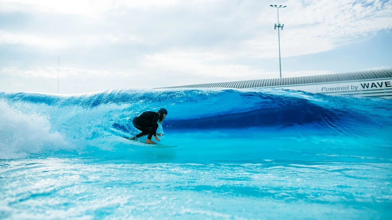 Surfer riding inside a blue wave at an artificial wave pool.