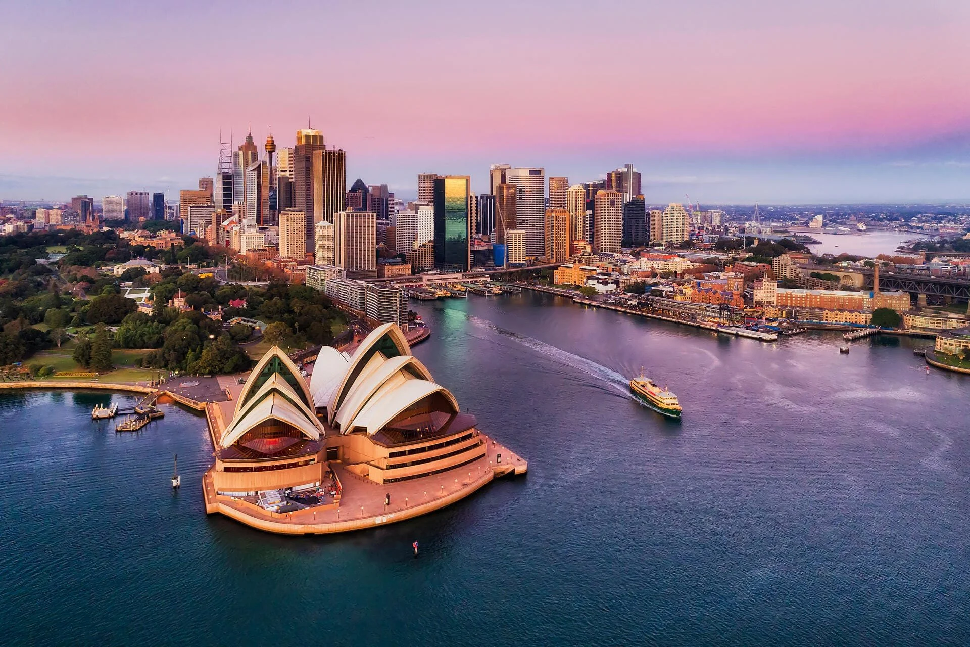 Aerial view of Sydney, Australia at dusk showcasing the Sydney Opera House in the foreground, the Sydney skyline with high-rise buildings in the background, and the water body with boats.