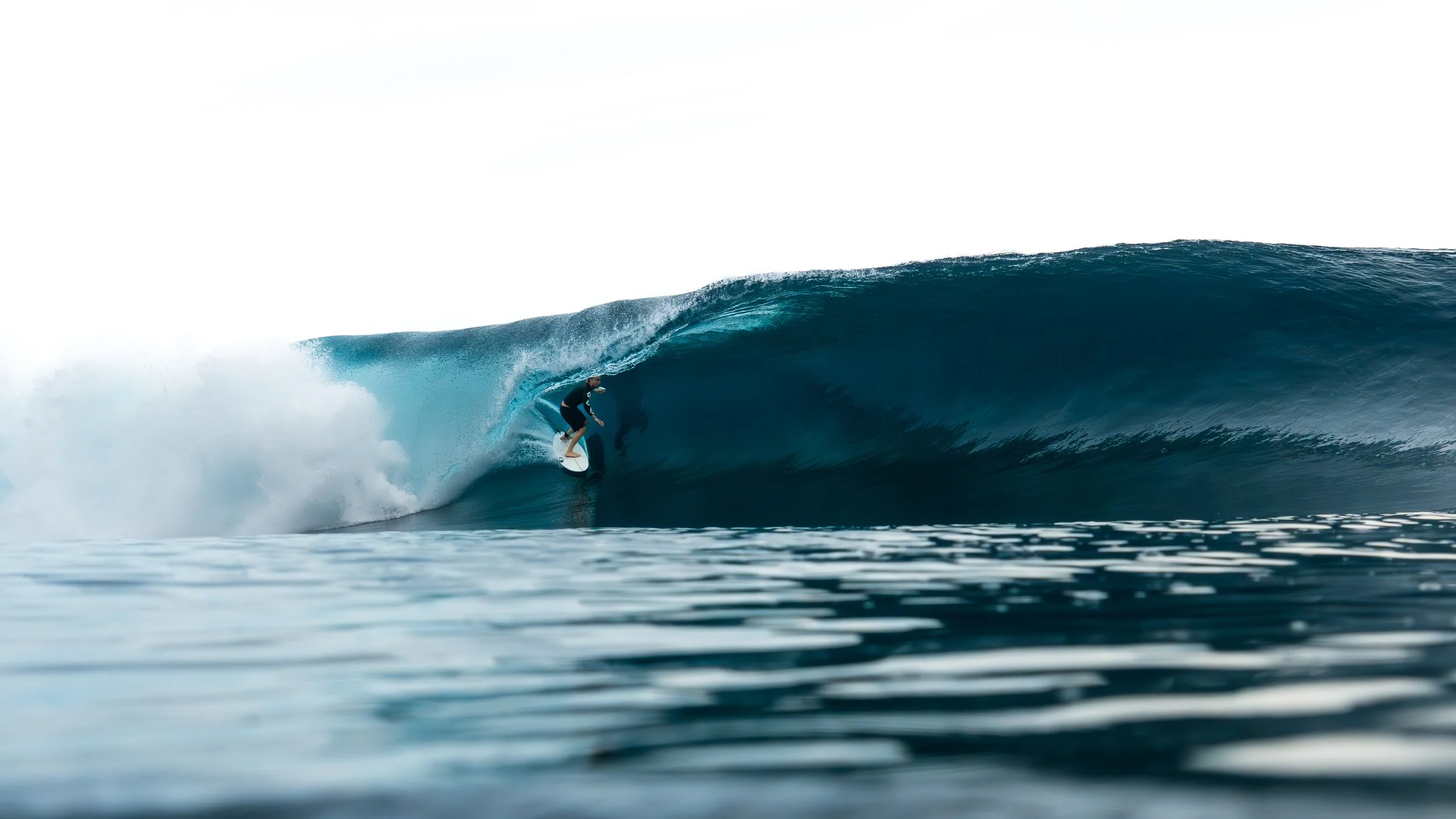 A person surfing on a large blue wave in the ocean.