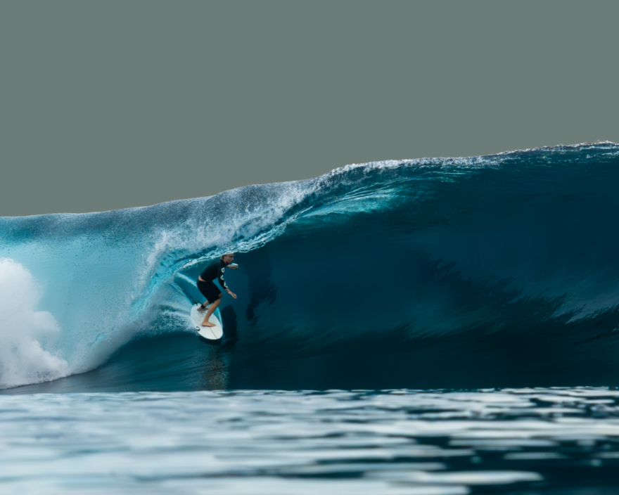 A person surfing on a large ocean wave with a gray sky background.