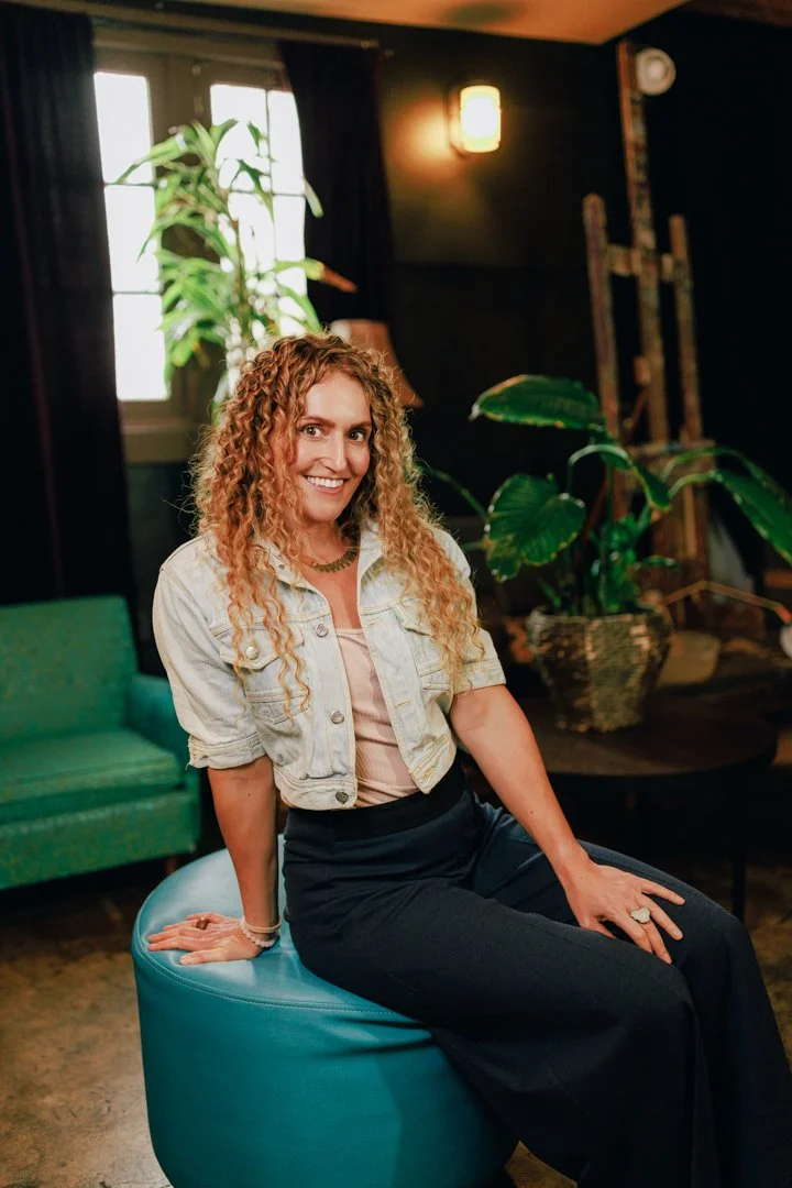 women sitting on seat with curly hair smiling at camera with plants in background