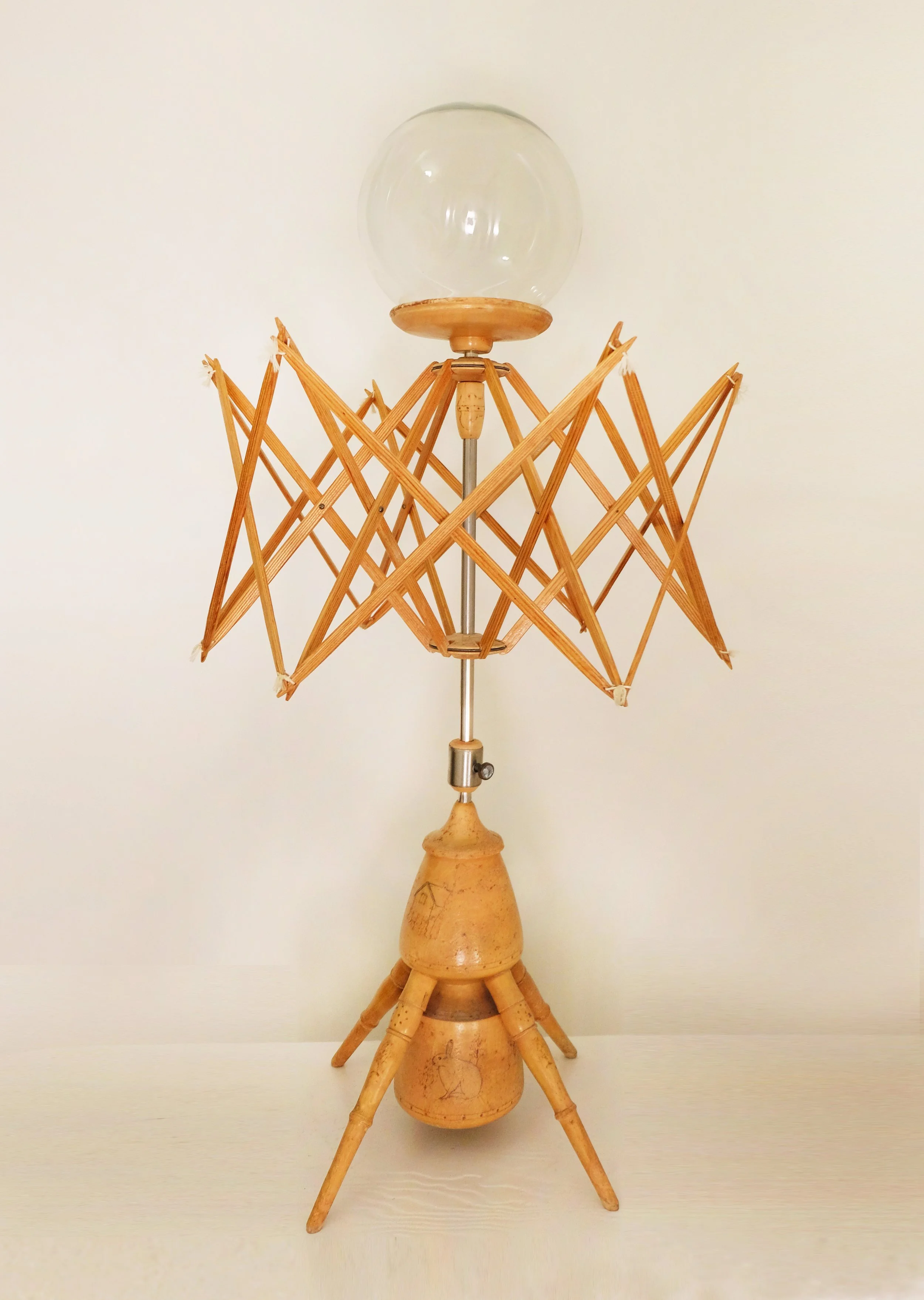 ALIEN, 2026, 93x50x50cm. Skulptur av hespetre og lampeskjerm

Skulpturen består av husholdningsobjekter kombinert til å minne om en liten skapning med astronauthjelm. Hespetreet er et arveobjekt, og inneholder et antall illustrasjoner fra 1973 som er