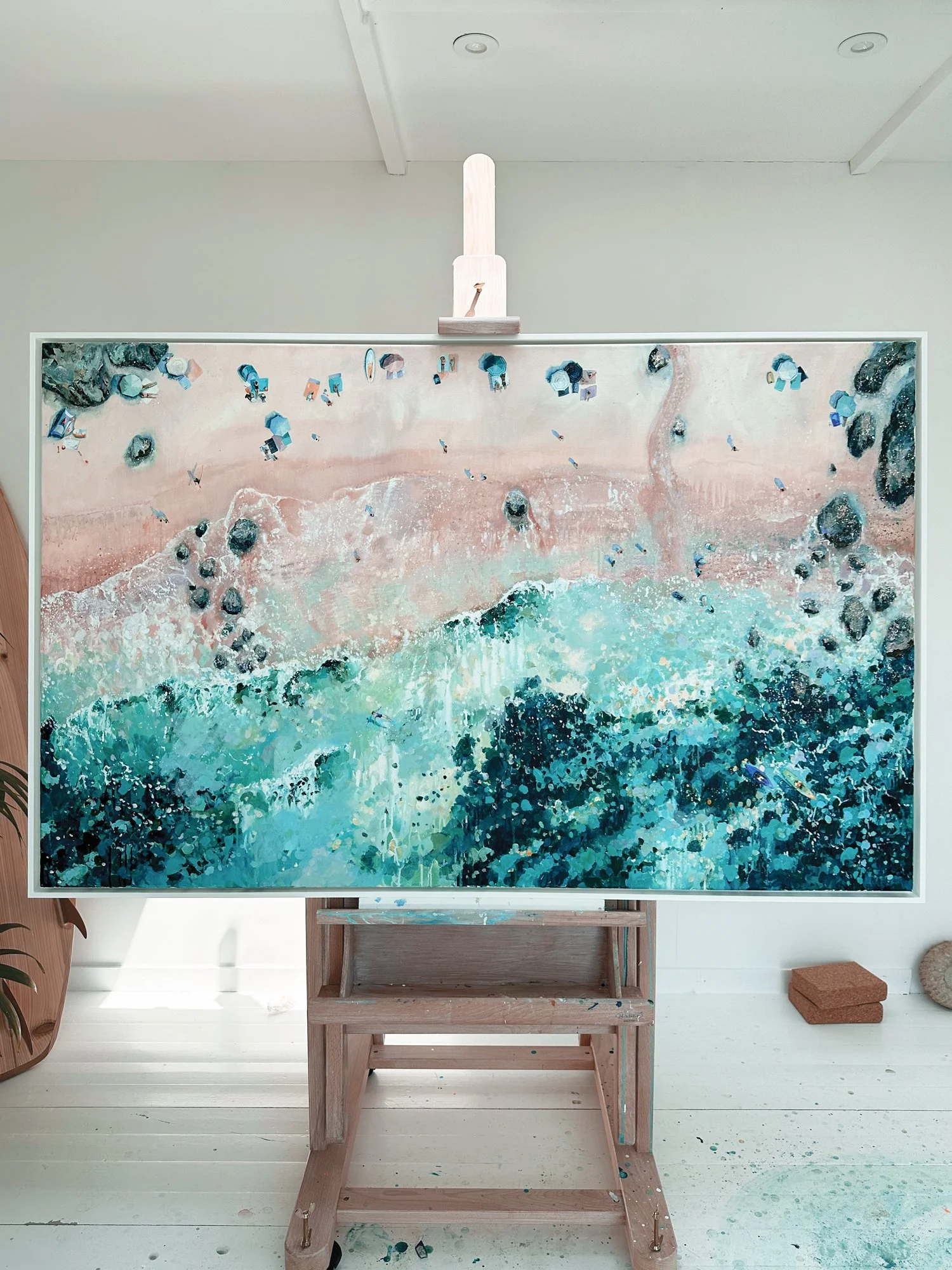 Large original aerial acrylic painting 'Shifting Tides' by Lucy Young. Features powerful crashing waves on a Dorset beach with colourful parasols and people by the rocks.