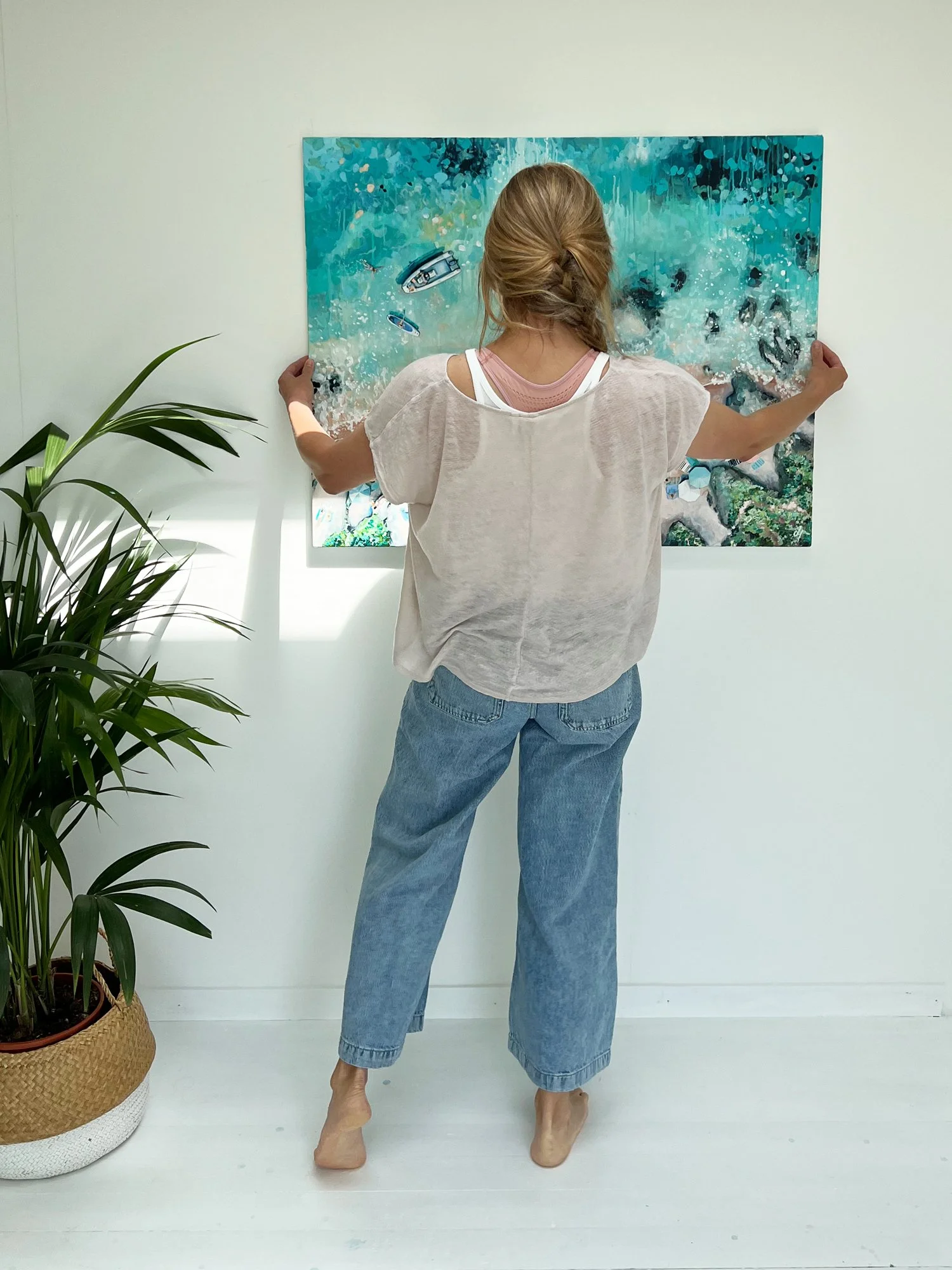 Artist Lucy Young hanging a finished, framed aerial seascape painting in her South West studio, ready for a private collector.