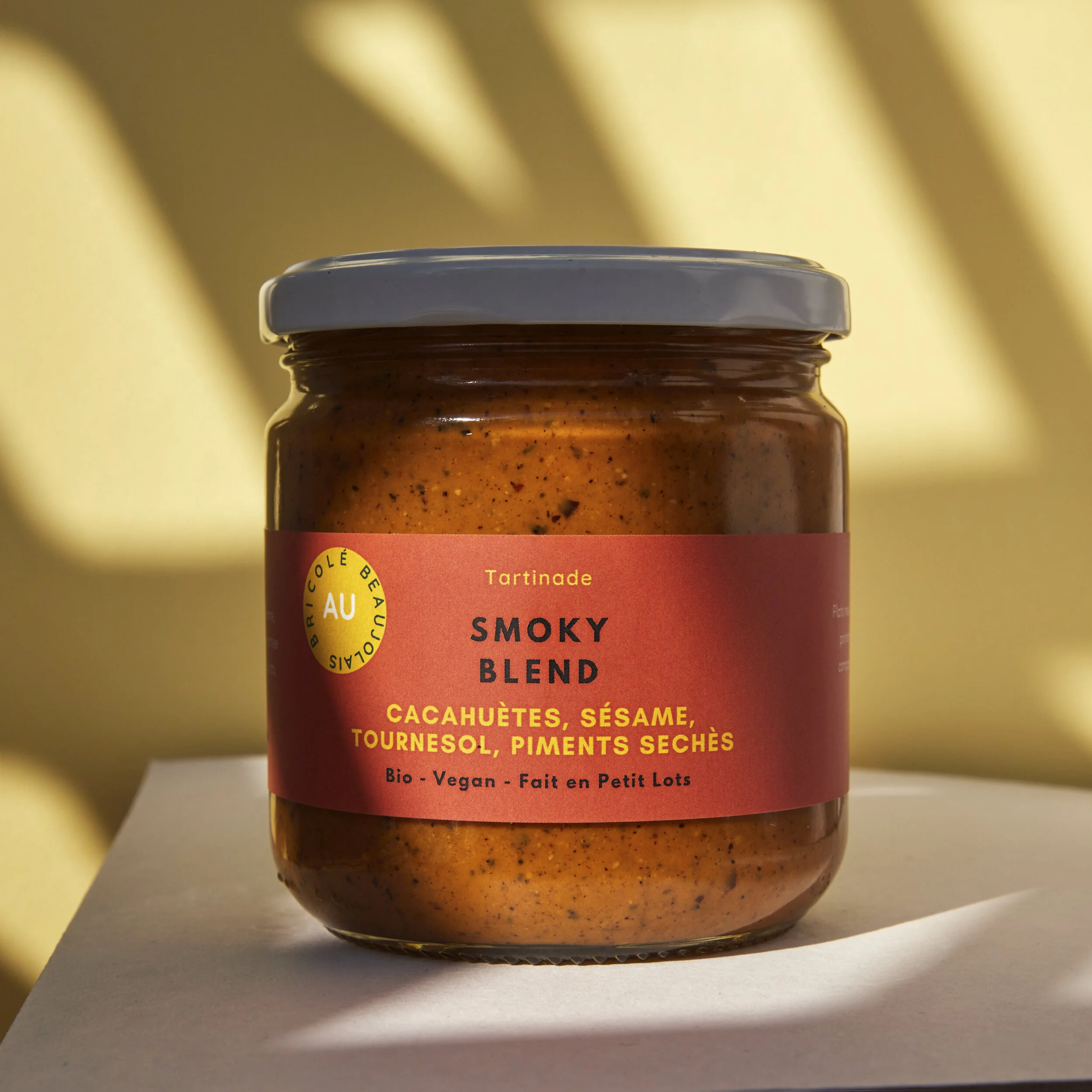 Jar of smoky spicy chili paste with a white lid and orange label, placed on a white surface.