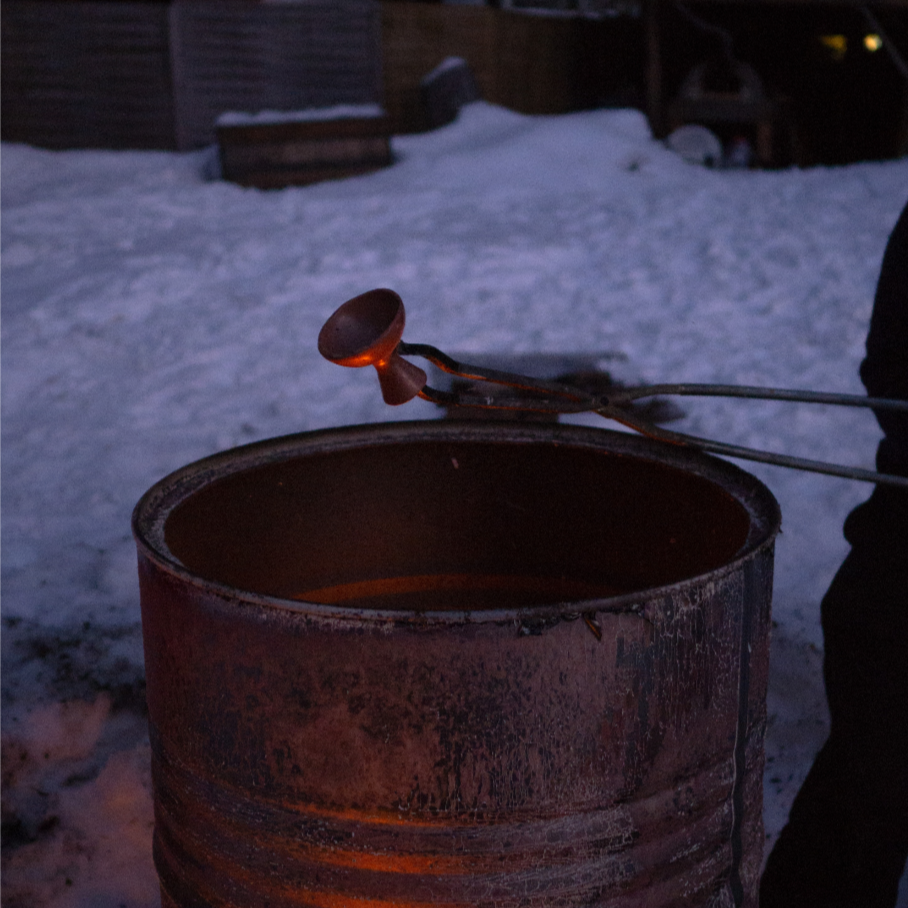 A fire pit with a fire poker resting on its edge, set outside in a snowy yard during dusk or early evening.