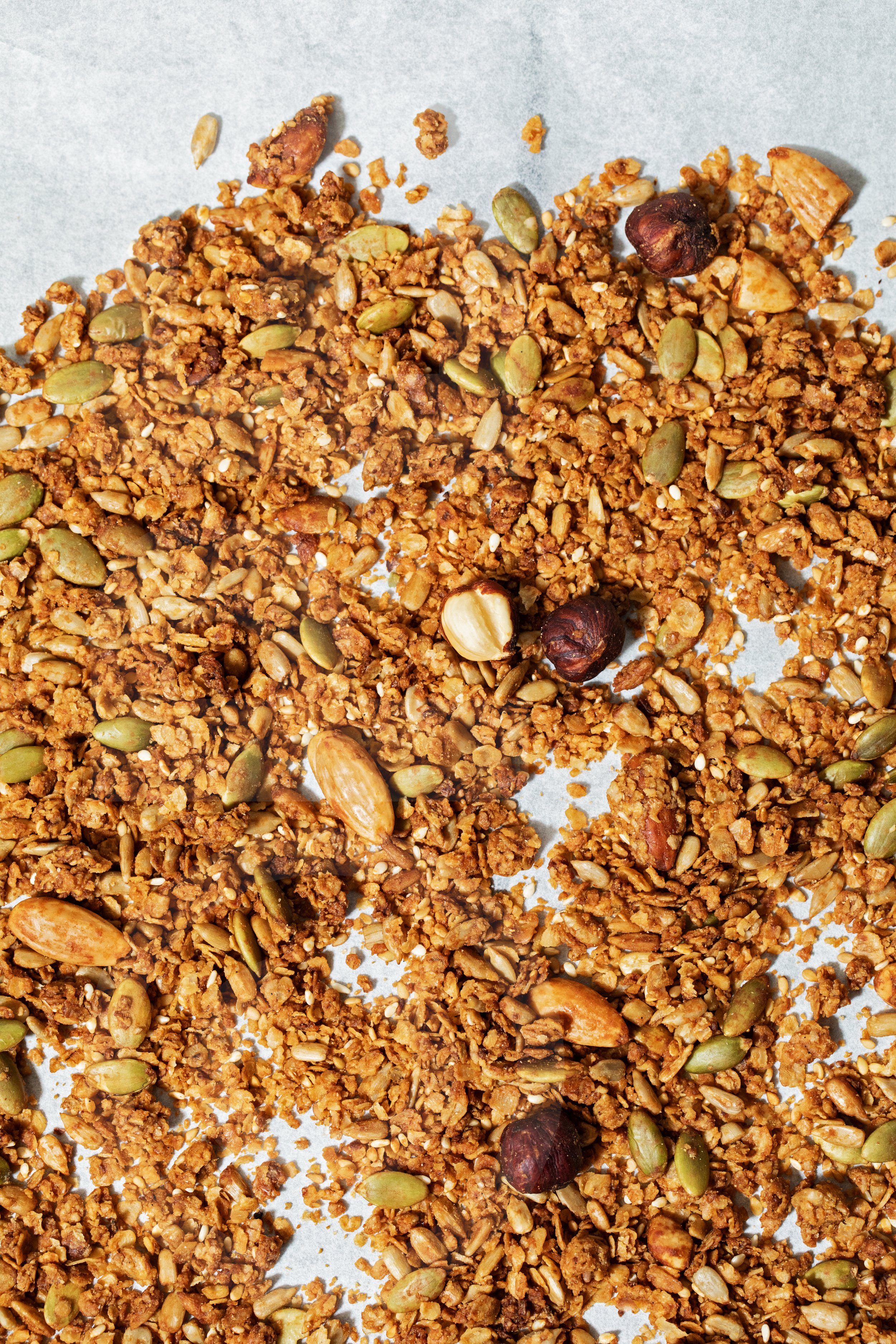 Spread granola containing pumpkin seeds and hazelnuts on white paper.