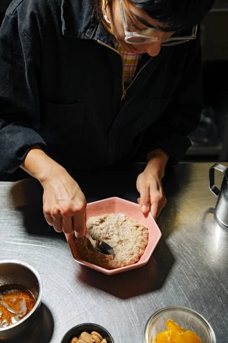 Person mixing dry ingredients in a pink bowl in a kitchen.