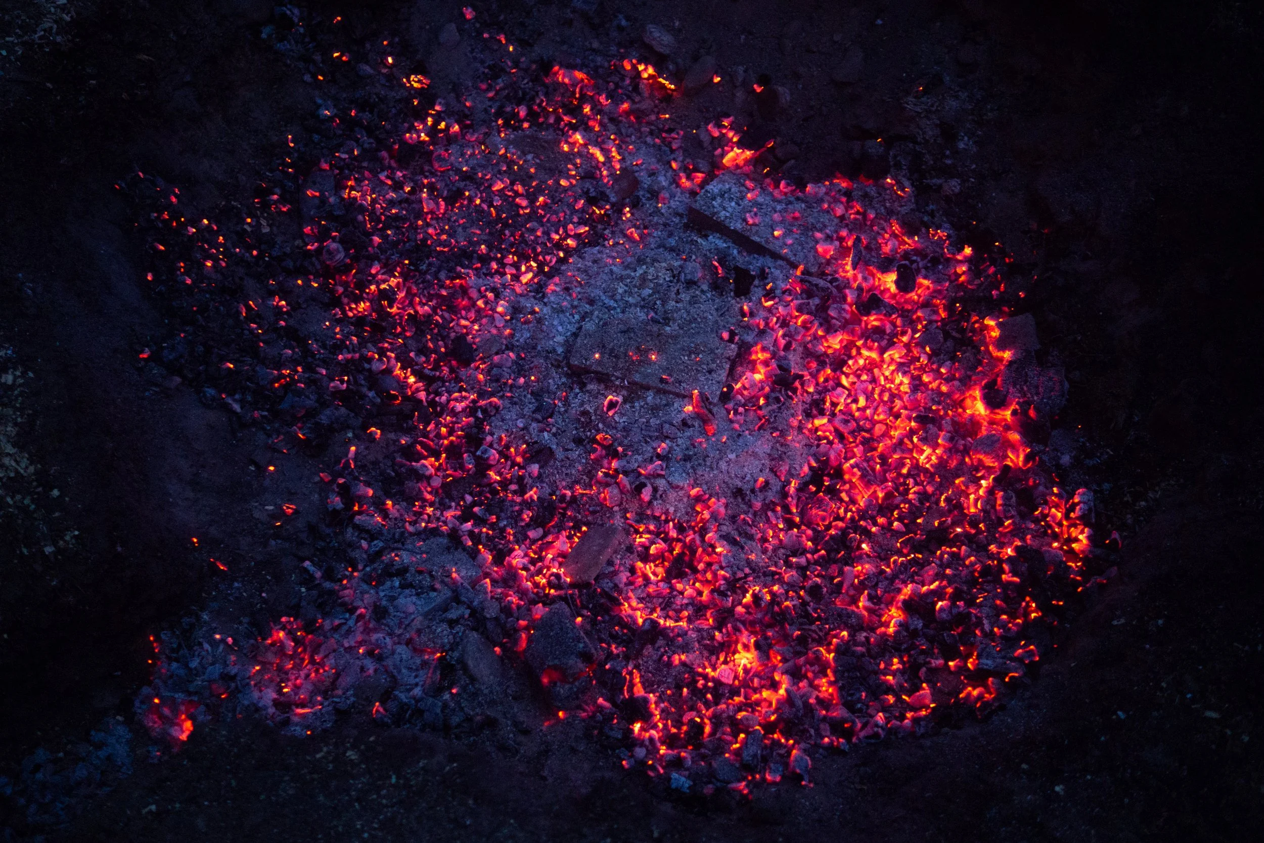 Glowing red hot embers and ashes on a dark surface.