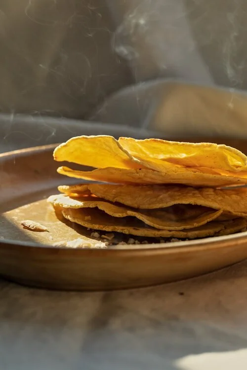 Stack of crispy tortilla chips on a plate with steam rising in the background.