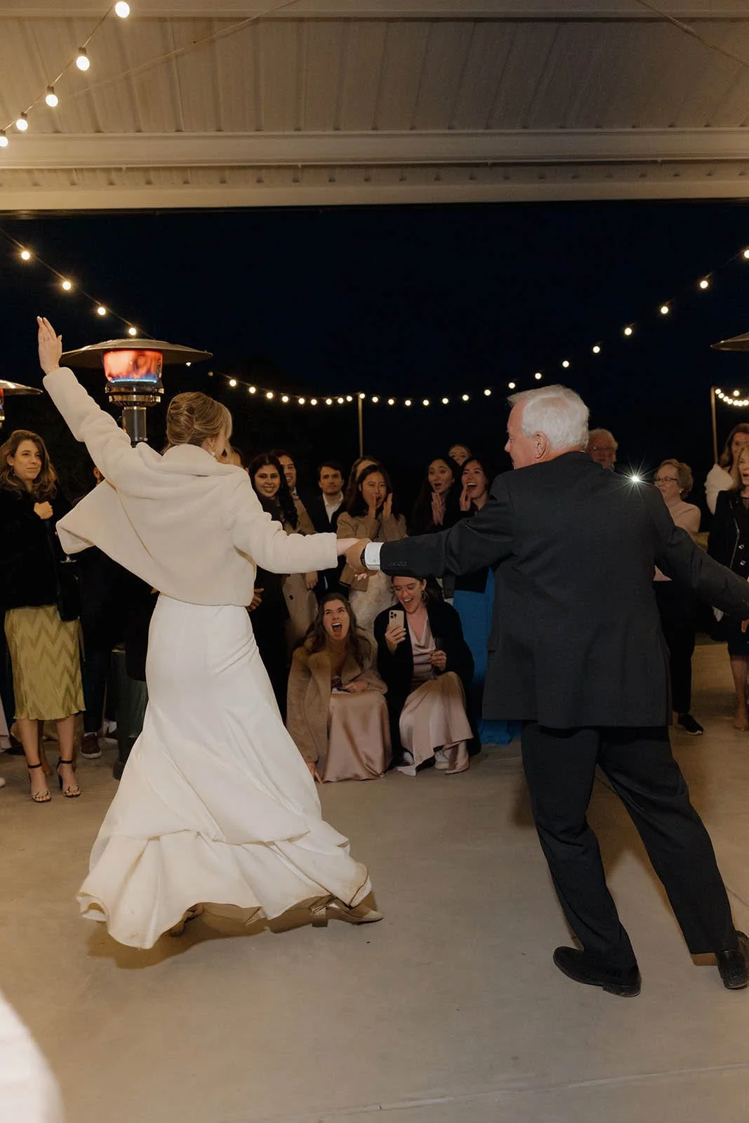Wedding reception with bride and groom dancing under string lights surrounded by guests