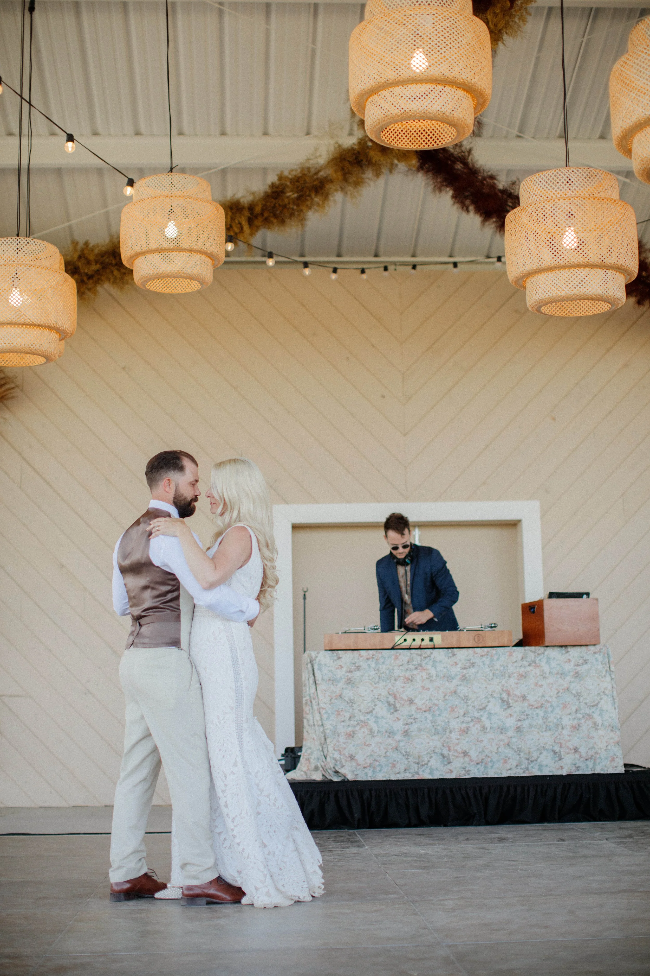 A couple sharing a dance at their wedding reception with a DJ playing music in the background.