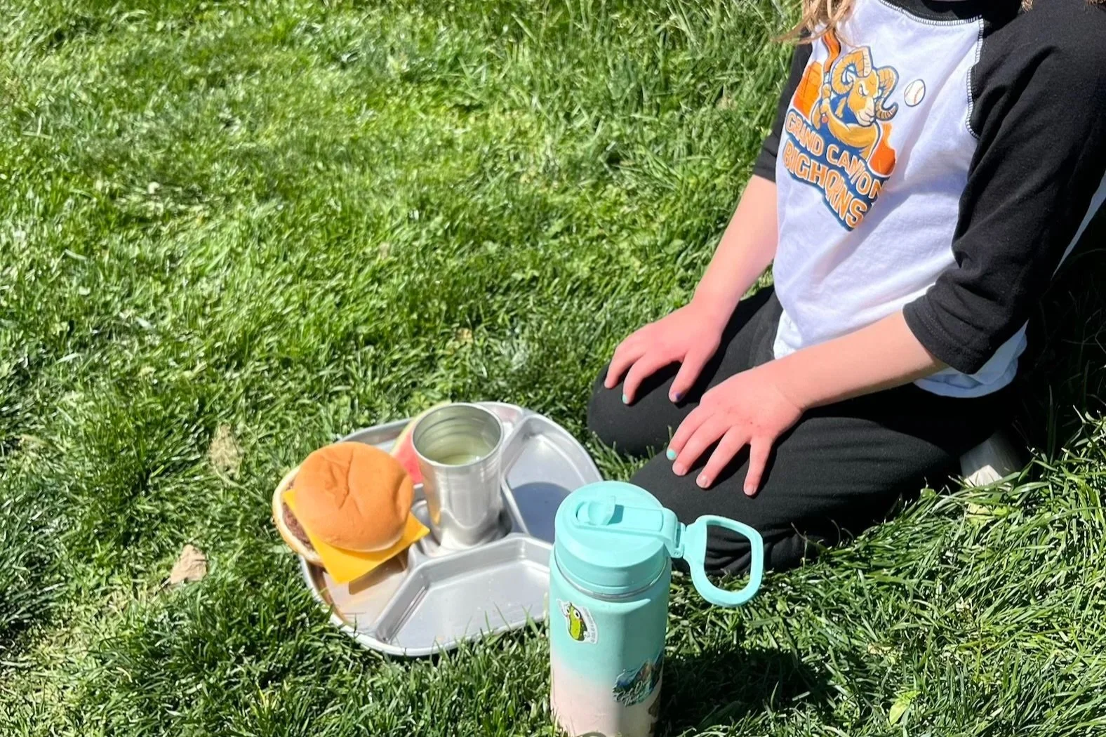 girl kneeling on the grass with lunch on a stainless steel tray