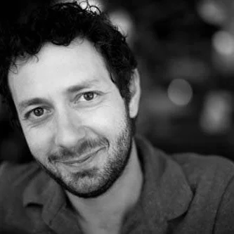 Black and white portrait of a man with curly hair and a beard, smiling slightly.