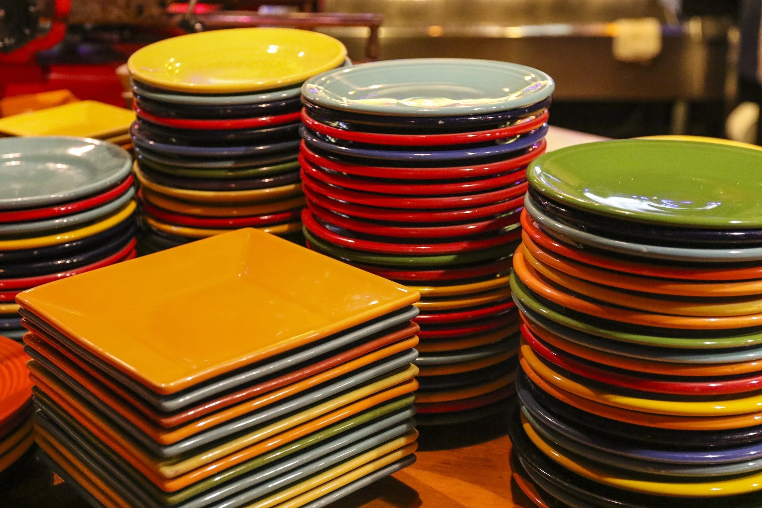 Stacks of colorful ceramic plates in yellow, red, green, black, and blue, arranged in circular and square shapes on a table.