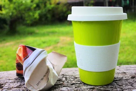 a crumpled paper cup next to a reusable cup