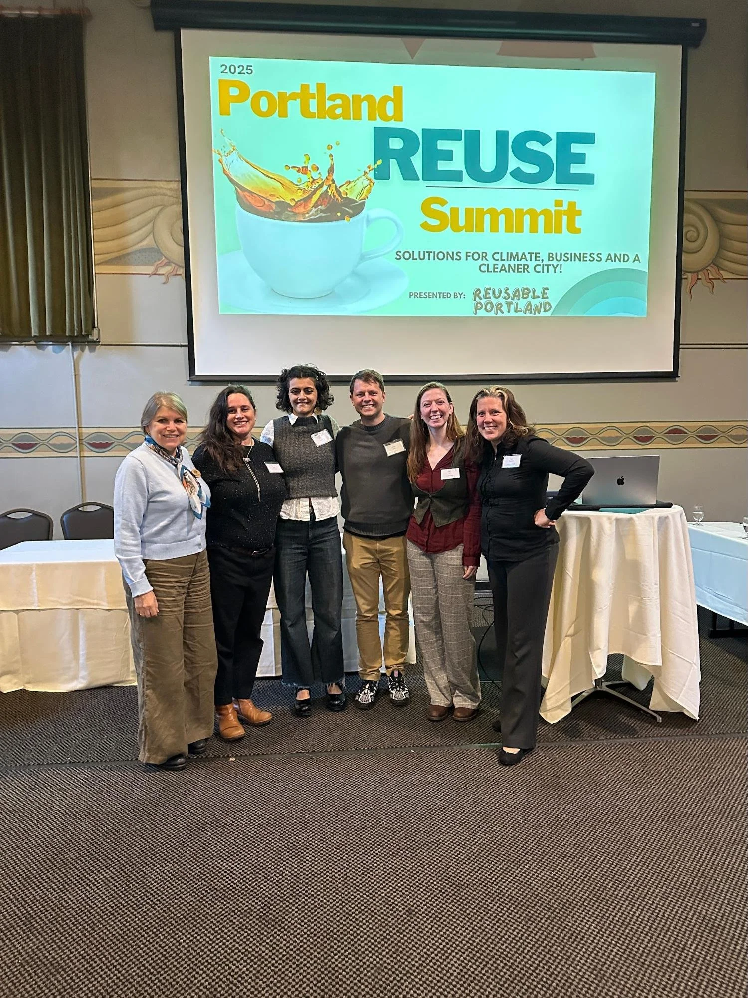 a group of women standing in front of a banner saying Portland Reuse Summit