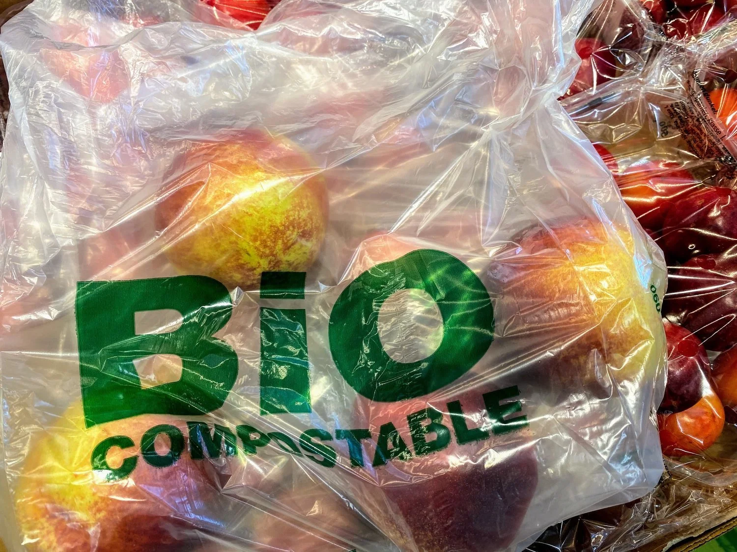 A plastic bag with the words 'BIO COMPOSTABLE' containing several apples, which are also visible outside the bag.