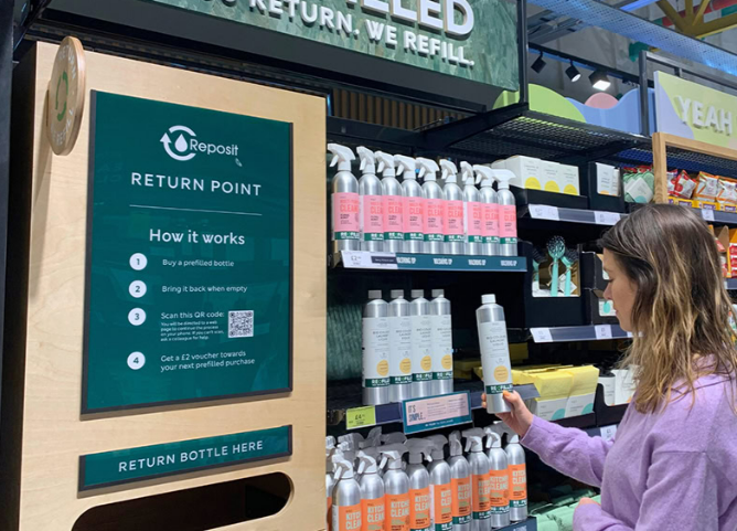 A woman taking a returnable refillable bottle of shampoo off a shelf in a grocery store