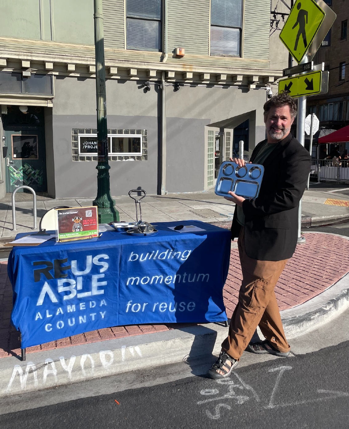 a man holding a stainless steel lunch tray in front of a campaign table