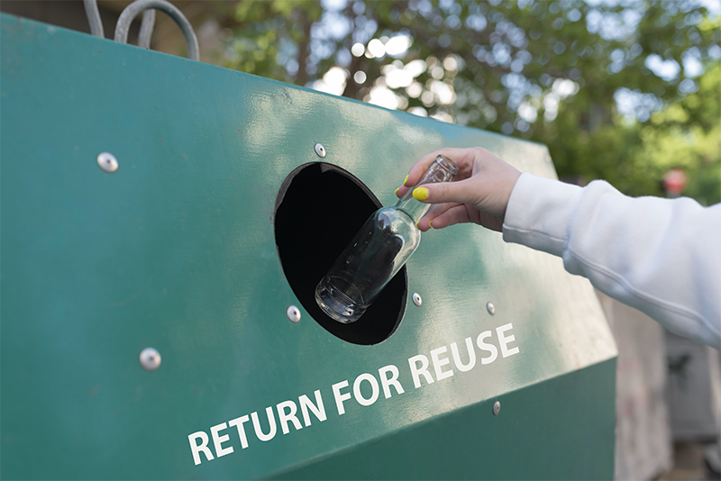 hand dropping empty glass bottle into a bottle return station