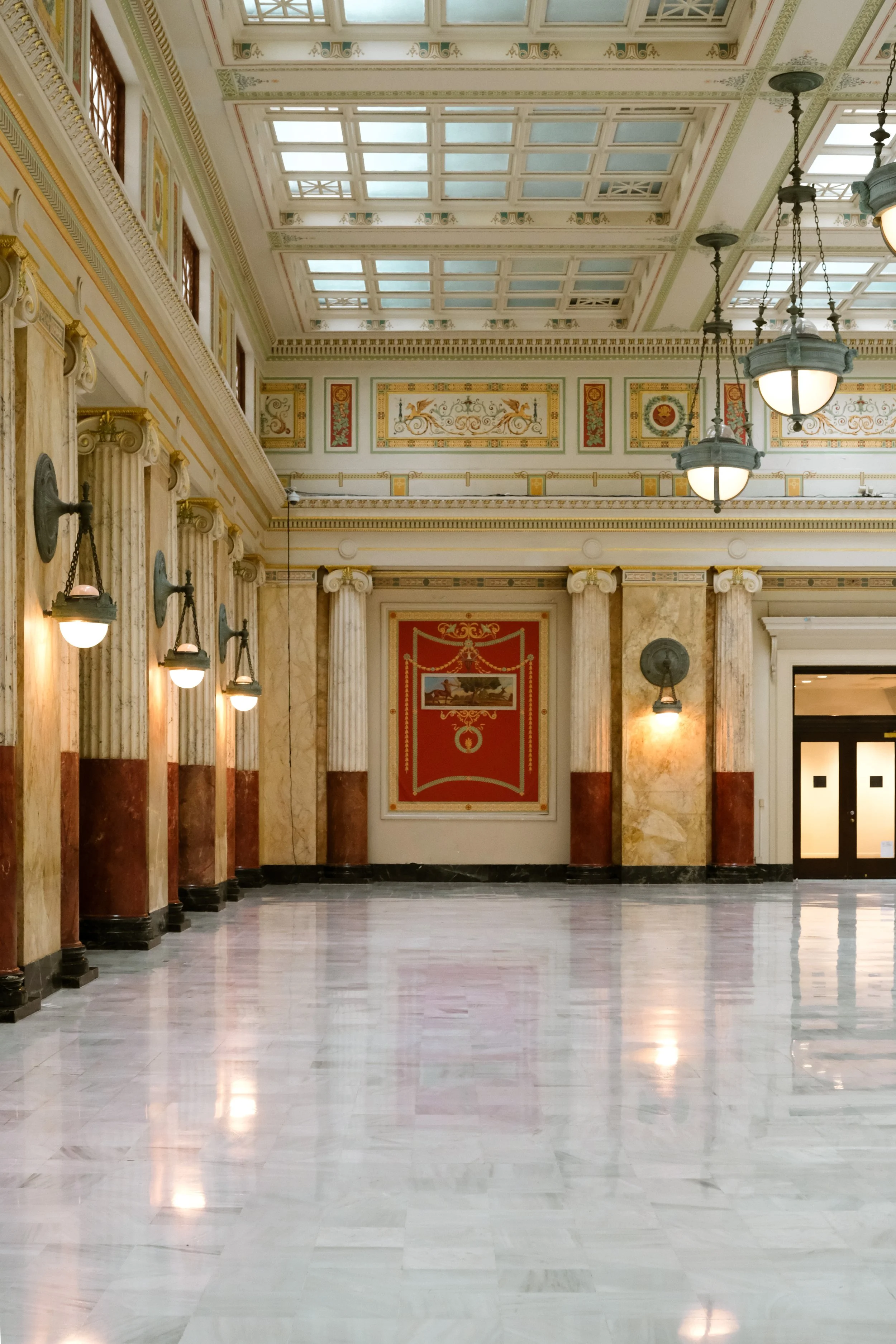 Elegant grand hall interior with marble floors, ornate columns, decorative wall panels, and hanging light fixtures in the historic Union Station building in Washington, DC.