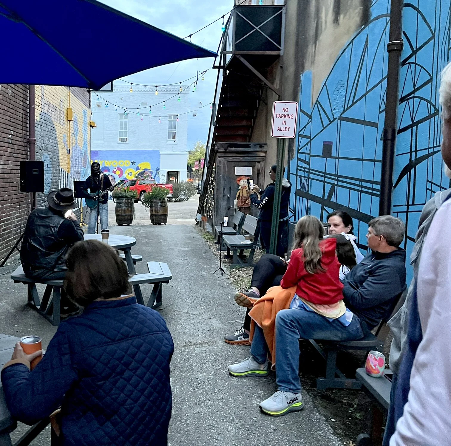 Live blues performance in Uptown Alley in downtown Brownsville, Tennessee, with people seated on benches and picnic tables enjoying the music.