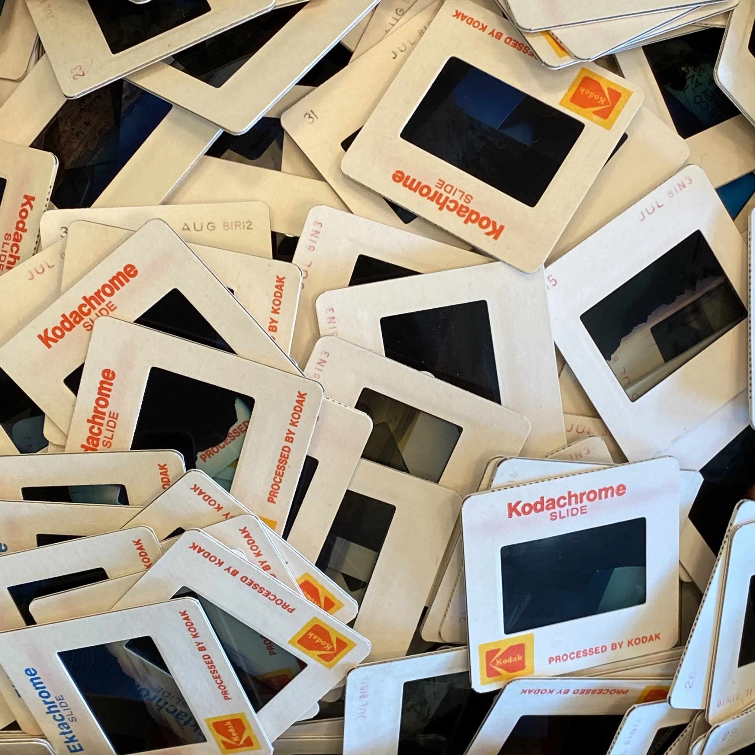 A collection of vintage Kodachrome slides scattered in a pile, featuring labels like "Processed by Kodak" and the Kodak logo in orange and yellow.