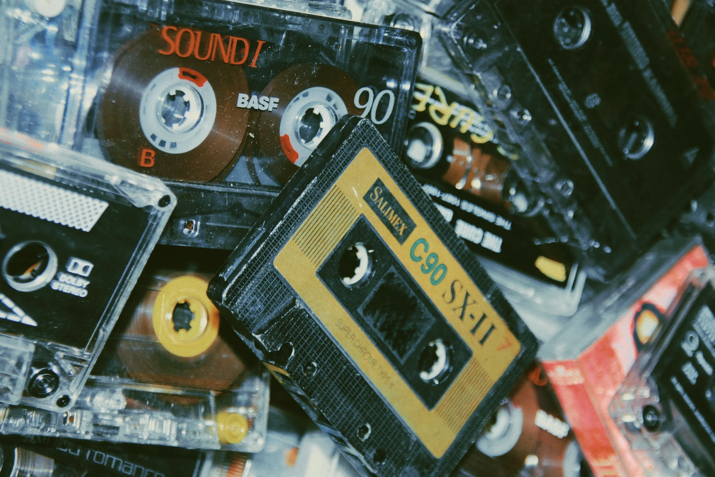 A collection of vintage audio cassette tapes, stacked haphazardly, with visible labels like "Salmex C90 SXII 7" and "BASF 90," evoking nostalgia for the cassette era.