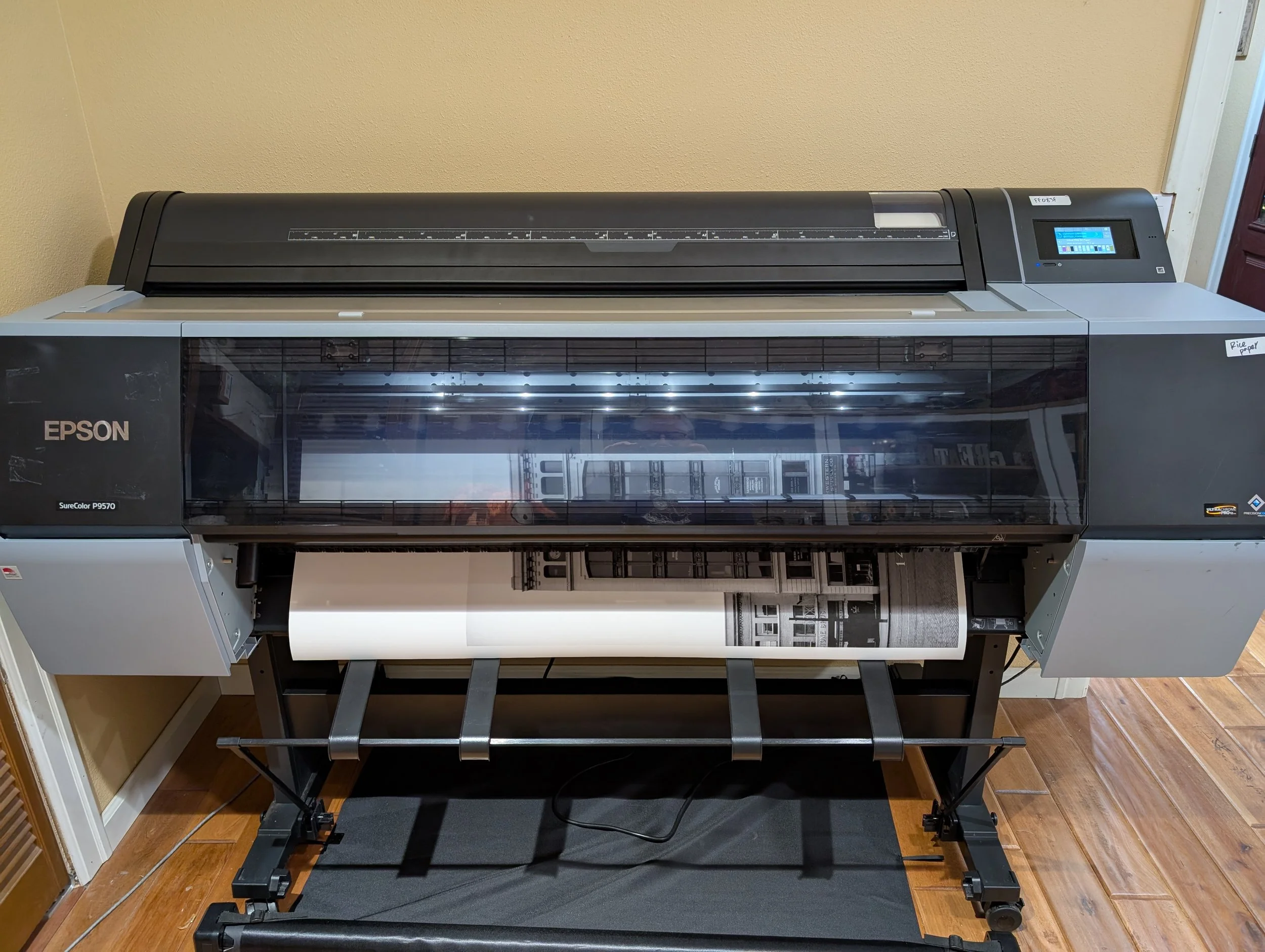 Professional Epson SureColor P9570 fine art printer outputting a large-format black-and-white panoramic photograph onto roll paper.