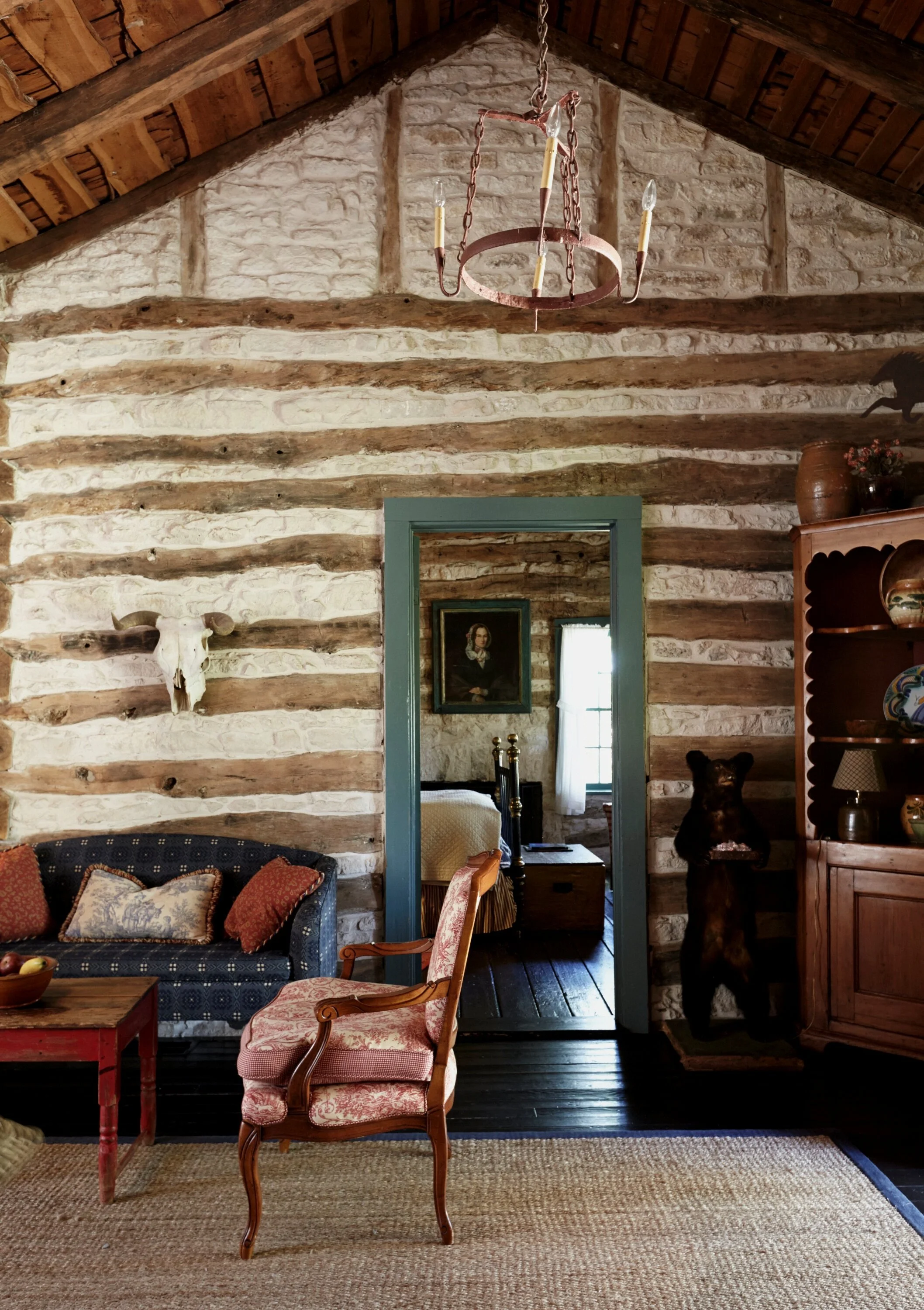 stone wall inside of cabin with green trim and vintage chair and couch