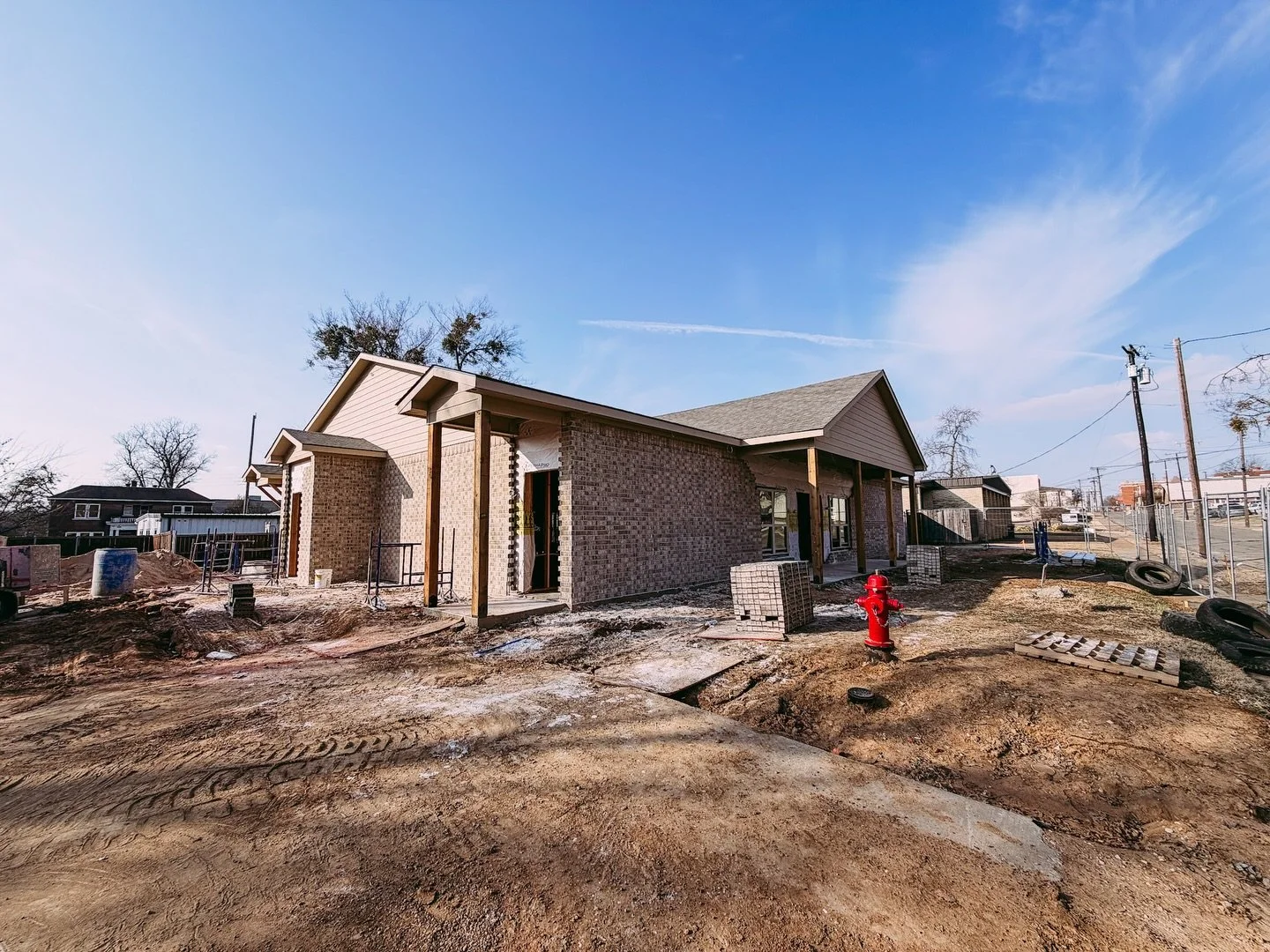 Exterior view of the new Paris Pregnancy Center under construction in Paris, Texas. The building features light brown brickwork, a neutral-toned roof, and wooden porch supports. The surrounding ground is undergoing active site work with a bright red 