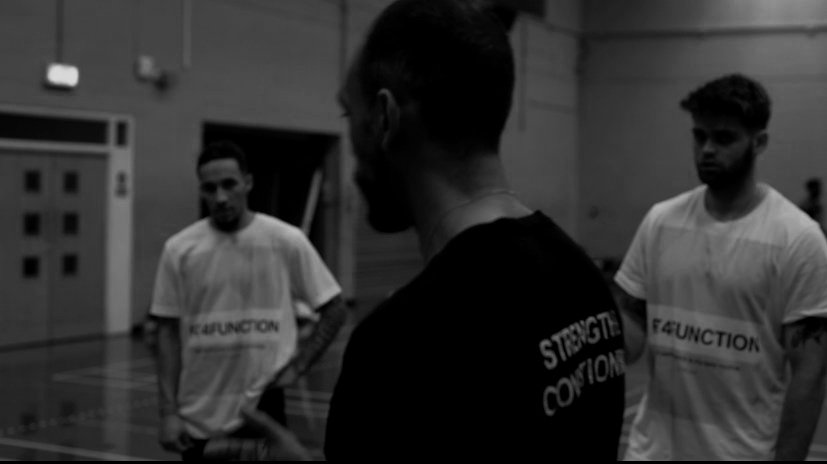 Three young men in sportswear standing in a gym, engaged in conversation.