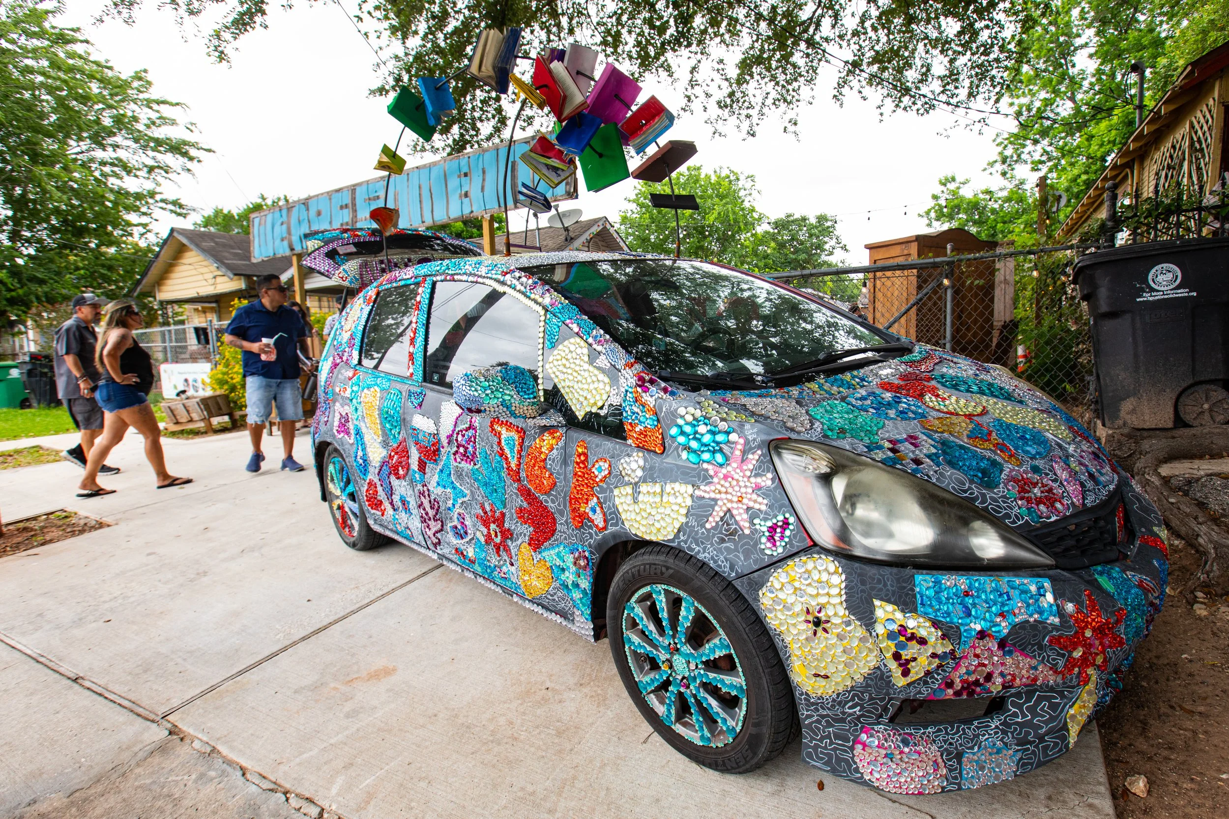Colorfully decorated car covered with mosaic artwork, parked on a residential street during the day.