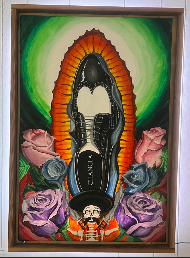A colorful painting of a black Oxford shoe with the word "chancla" inside, set against a radiant orange and green background with pink and purple roses at the bottom and a small skeleton figure at the base.