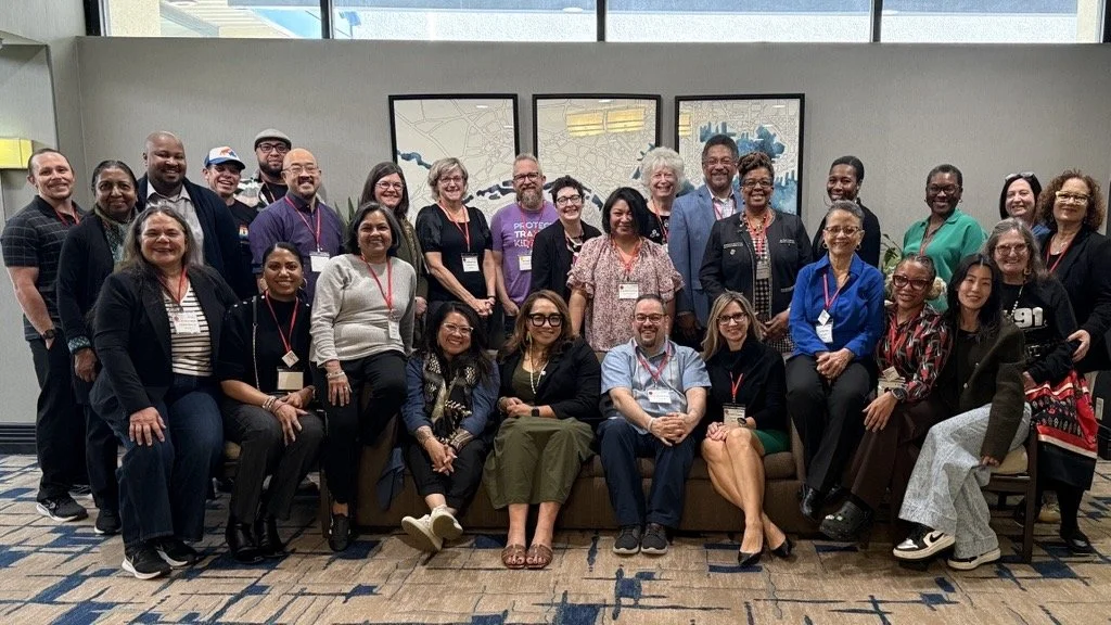 participants of the DEI roundtable wearing name badges pose together indoors for a group photo, smiling