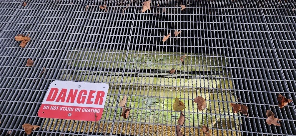 View through a light shaft onto the graffiti-covered Freedom Tunnel beneath Riverside Park in Manhattan, New York. A sign on the grate reads: “DANGER — DO NOT STAND ON GRATING.”