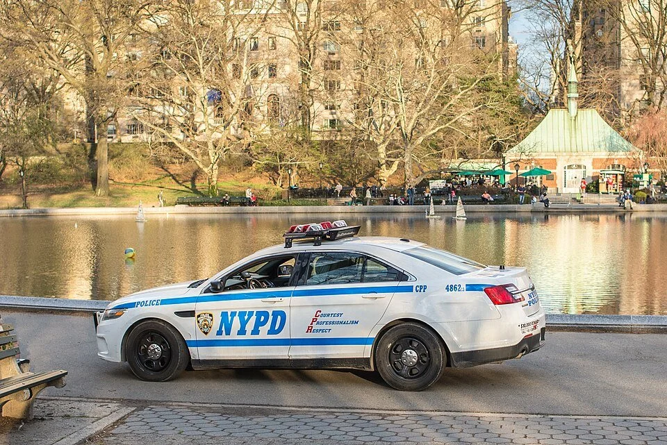 NYPD police car patrolling a tree-lined road in Central Park.