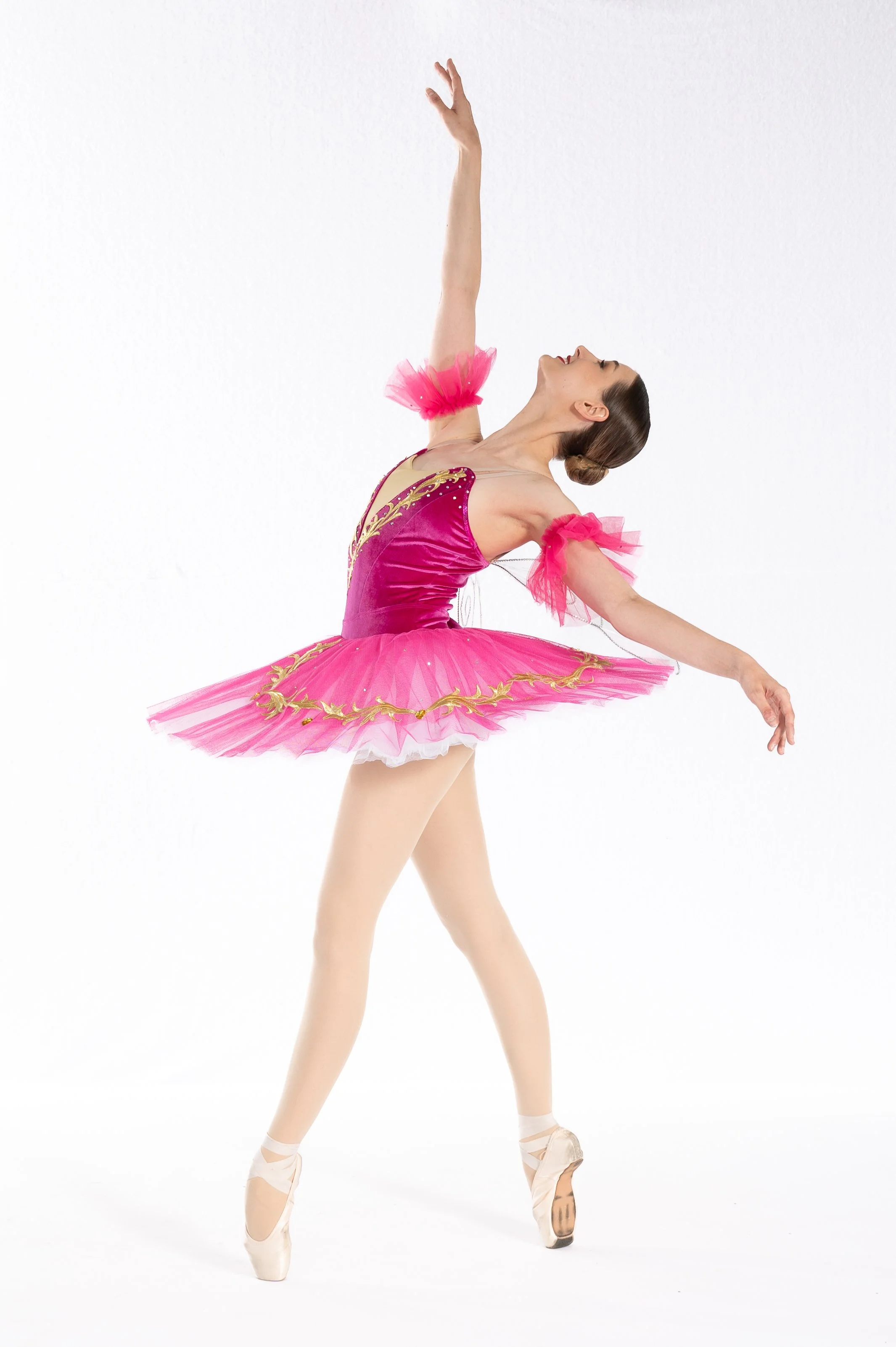 Ballet dancer in a pink tutu performing a pose on stage, arms raised and head tilted back.dance photo day with Marina Birch Photography