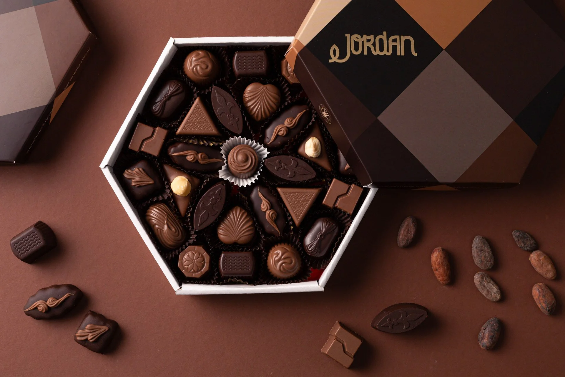 Open box of assorted chocolates on a brown surface, with some chocolates spilled around, an opened black and brown checkered box with 'Jordan' written on it.  Photo by lucie lizlerova