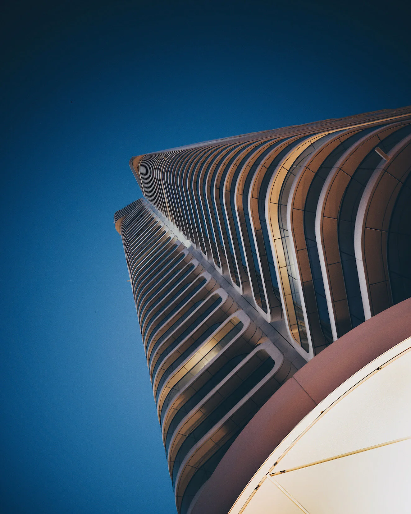 Aufnahme eines modernen Hochhauses bei Nacht mit wellenförmigem Fassadendesign und beleuchteten Fenstern, Blick von unten nach oben gegen dunklen Himmel