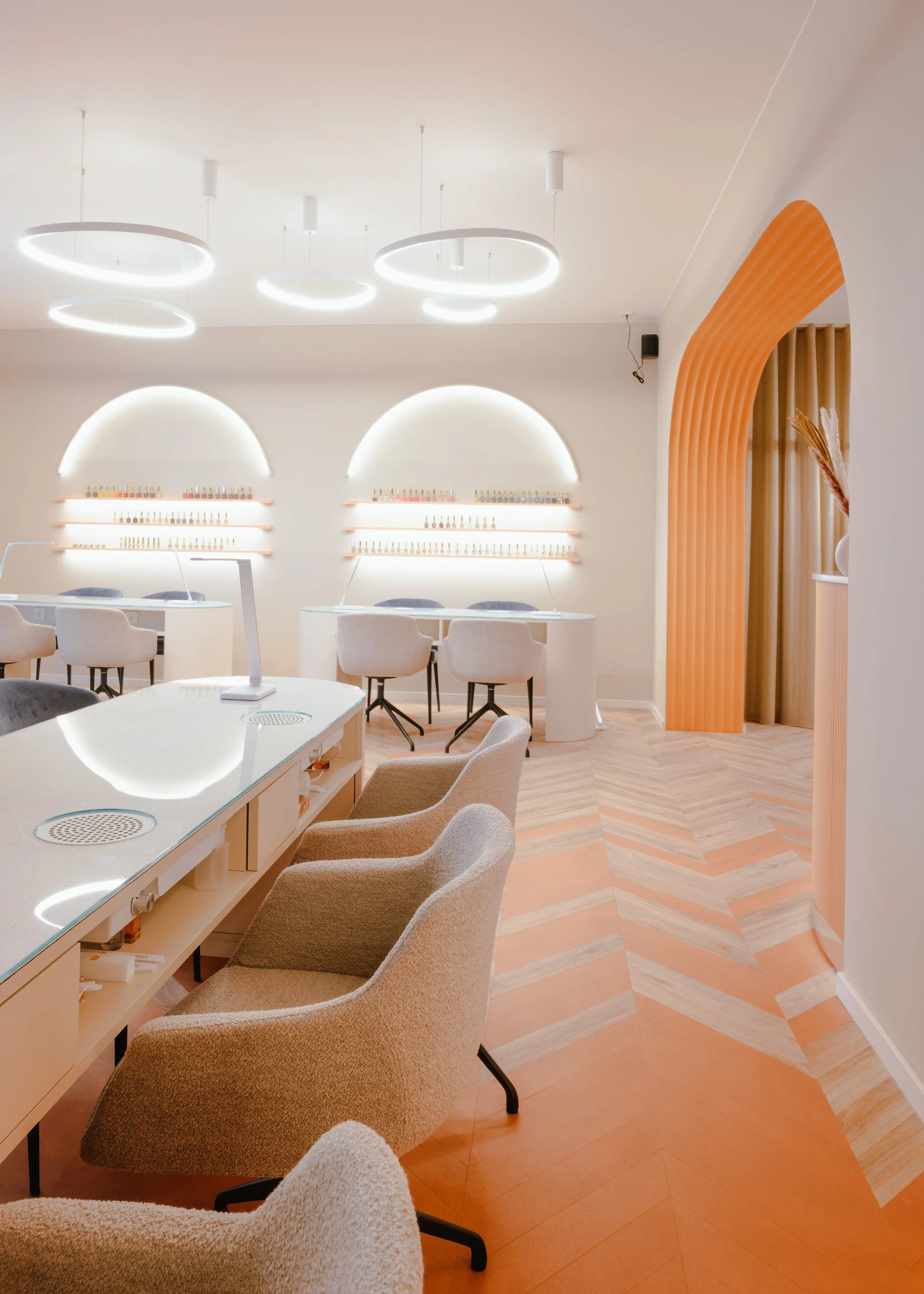 Innenraum eines modernen, minimalistisch gestalteten Raums mit beigefarbenen Sesseln, weißen Tischen, beleuchteten Regalen und stilvollem Lichtdesign.