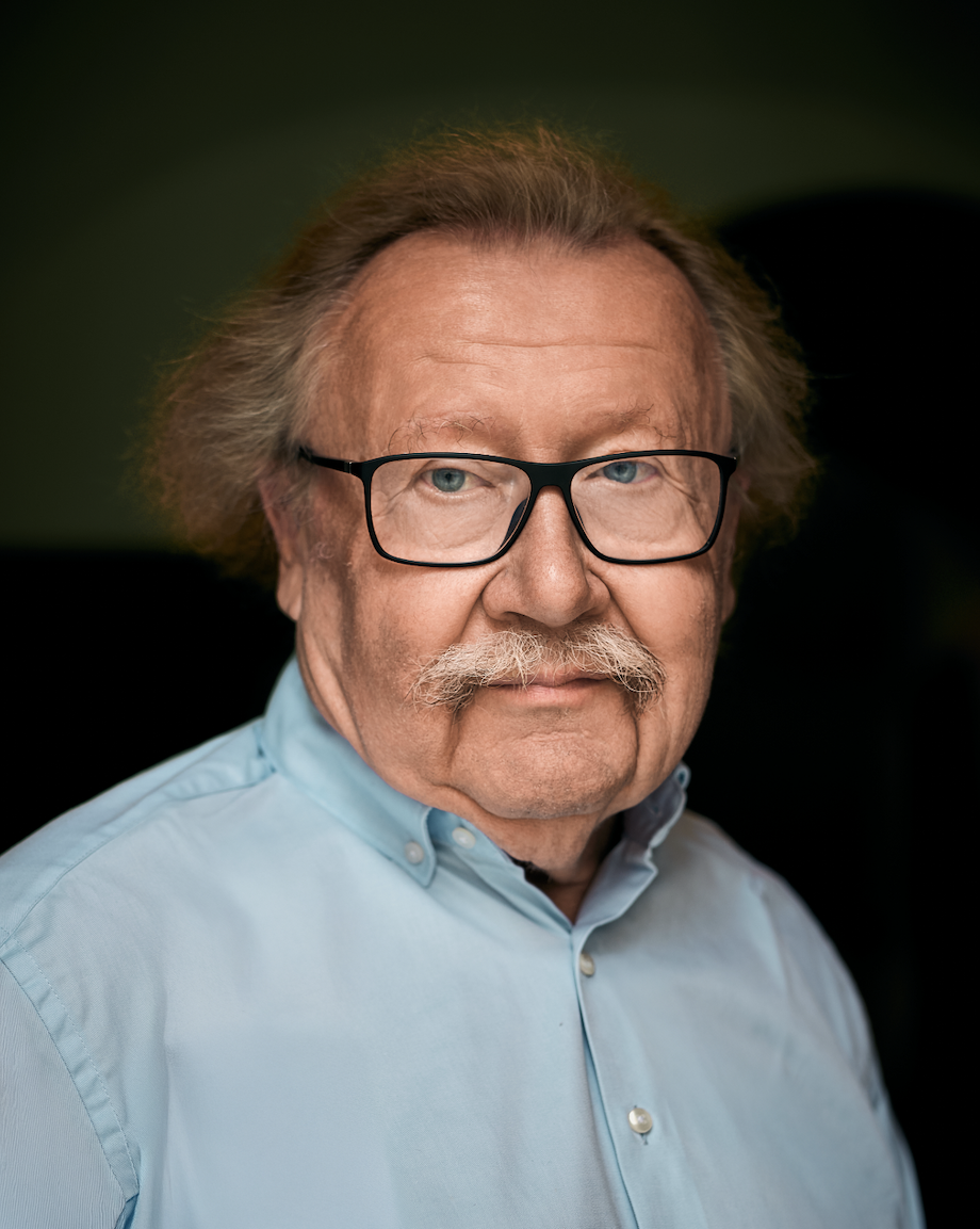 Philiosoph Peter Sloterdijk eines alten Mannes mit braunem, welligem Haar, Brille und Schnurrbart, trägt ein hellblaues Hemd, vor dunklem Hintergrund.
