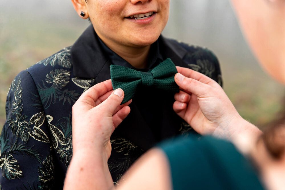Bride wearing a bowtie as it's getting adjusted by her partner at their elopement in the mountains