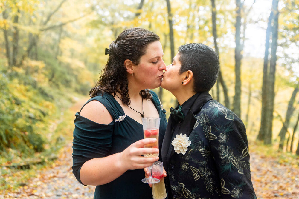 Wedding couple kissing while holding champagne flutes surrounded by nature in Asheville, NC
