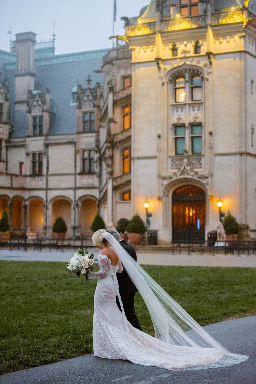 bride and her father walking together in front of the biltmore estate for her wedding